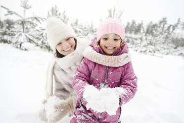 Glückliche Mutter und Tochter spielen mit Schnee im Winterpark - EYAF02955