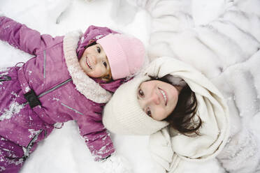 Happy daughter lying on snow with mother - EYAF02957