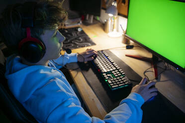 Junge trägt ein Headset und spielt ein Videospiel am Computer zu Hause - NJAF00790