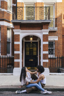 Carefree young couple sitting on ground in front of building - ASGF04873