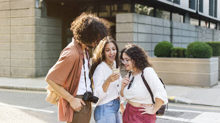 Junge Frau teilt Smartphone mit Freunden auf der Straße - ASGF04874