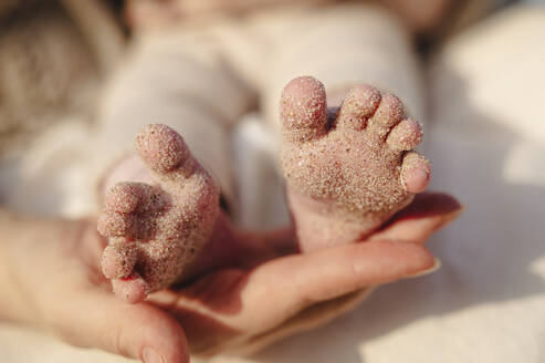 Mother holding baby girl's feet covered in sand - ALKF01005