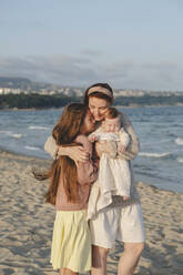 Happy mother embracing daughters at beach on sunny day - ALKF01012