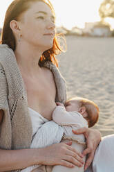 Woman breastfeeding baby girl at beach - ALKF01029