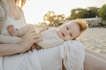 Baby girl lying on mother's lap at beach - ALKF01031