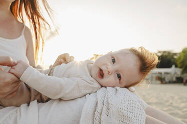 Cute baby girl lying on mother's lap at beach - ALKF01032