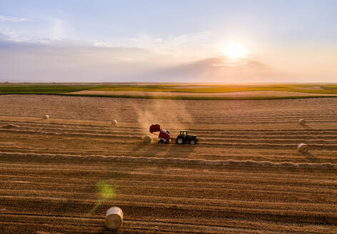 Tractor harvesting and baling wheat field at sunset - NOF00927