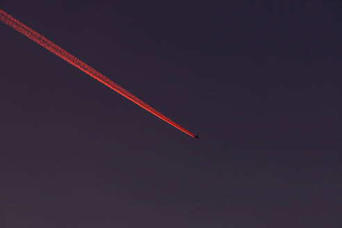 Airplane leaving red vapor trail against sky at night - NDF01606