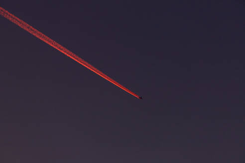 Flugzeug hinterlässt roten Kondensstreifen am nächtlichen Himmel - NDF01606