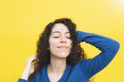 Frau mit verschiedenen Aufklebern im Gesicht vor gelbem Hintergrund - MGRF01078