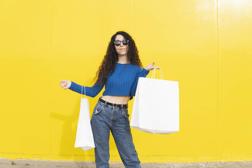 Frau mit weißen Einkaufstaschen vor einer gelben Wand stehend - MGRF01090