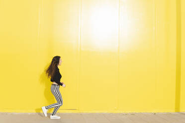 Woman in striped pants running near yellow wall - MGRF01099