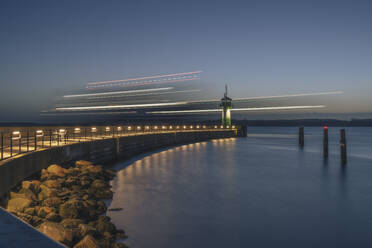 Germany, Schleswig-Holstein, Lubeck, Blurred motion of ship passing Travemunde lighthouse at dawn - KEBF02828