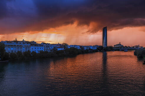 Spain, Andalusia, Seville, Guadalquivir river and surrounding buildings at stormy twilight - ABOF00958
