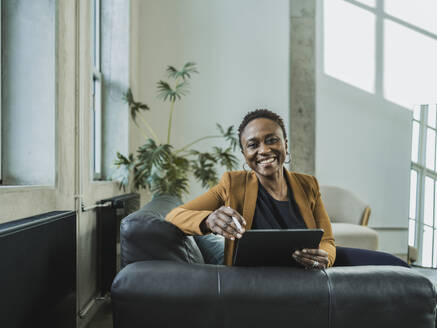 Lächelnde Geschäftsfrau mit Tablet-PC auf dem Sofa im Büro sitzend - MFF09558