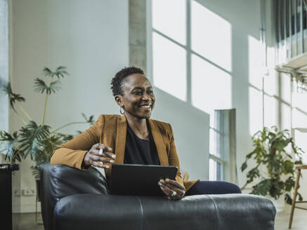 Mature businesswoman with tablet PC sitting on sofa at office - MFF09559