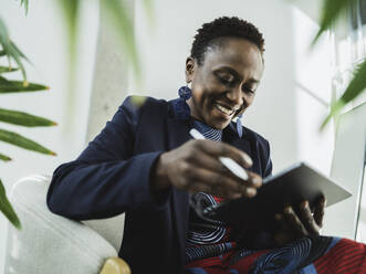 Lächelnde Geschäftsfrau, die im Büro sitzend einen Tablet-PC betrachtet - MFF09584