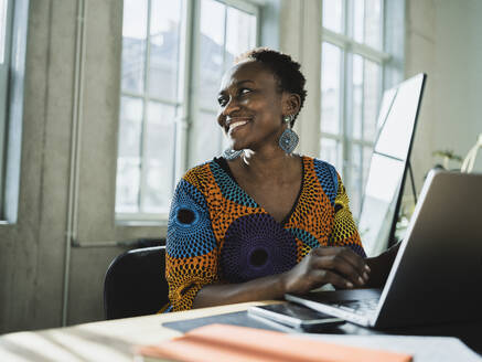 Lächelnde Geschäftsfrau mit Laptop am Schreibtisch im Büro - MFF09591
