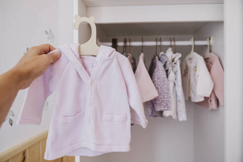 Hand einer Frau, die Babykleidung in der Nähe eines Kleiderschranks zu Hause hält - EBBF08666