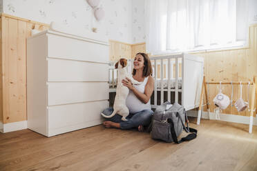 Glückliche schwangere Frau spielt mit Hund in Kinderzimmer Schlafzimmer zu Hause - EBBF08681