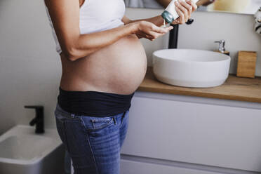 Schwangere Frau verwendet Creme auf dem Bauch im Badezimmer zu Hause - EBBF08694