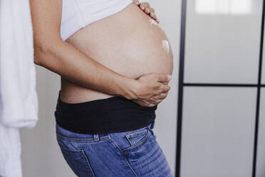 Schwangere Frau verwendet Creme auf Bauch zu Hause - EBBF08697