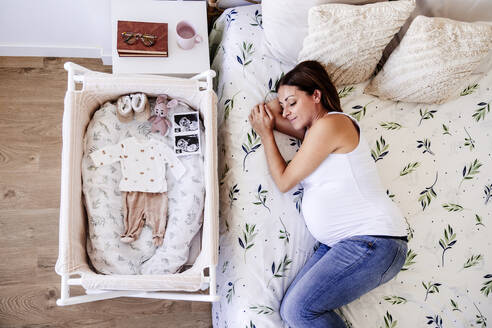 Schwangere Frau schläft auf dem Bett in der Nähe der Krippe zu Hause - EBBF08699