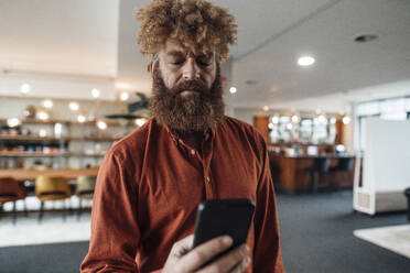 Geschäftsmann mit Afrofrisur, der in einer Büro-Cafeteria ein Smartphone benutzt - JOSEF23437