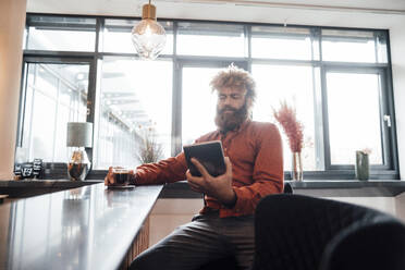 Älterer Geschäftsmann, der in einer Büro-Cafeteria sitzt und einen Tablet-PC benutzt - JOSEF23448