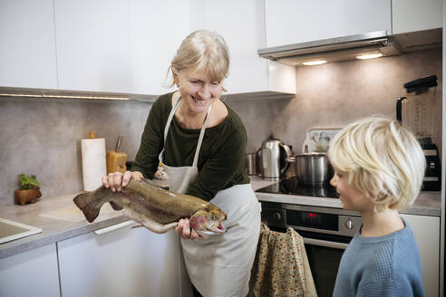 Ältere Frau zeigt ihrem Enkel in der Küche zu Hause Fisch - NJAF00798