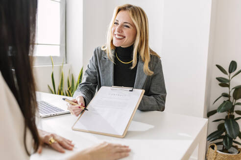 Smiling businesswoman explaining contract to colleague at desk - XLGF03324