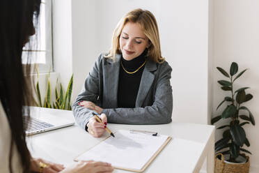 Smiling businesswoman discussing over contract with colleague in office - XLGF03327