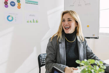 Cheerful businesswoman sitting at desk in office - XLGF03335