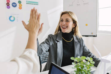 Happy businesswoman giving high-five to colleague at desk - XLGF03336