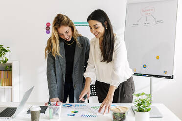 Smiling businesswoman discussing over charts and graphs with colleague in office - XLGF03343