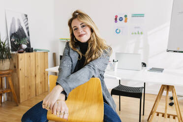 Smiling businesswoman sitting on chair near desk in office - XLGF03354