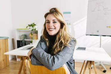 Happy businesswoman sitting on chair in office - XLGF03355