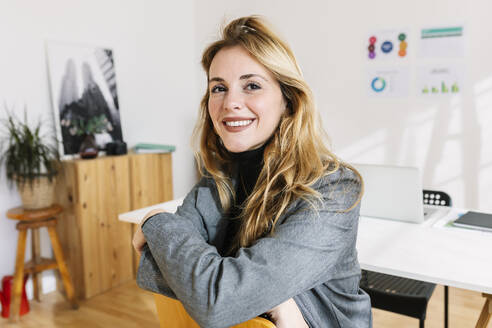 Smiling bond businesswoman sitting on chair in office - XLGF03356