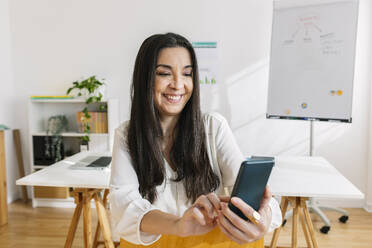 Smiling businesswoman using smart phone in office - XLGF03359