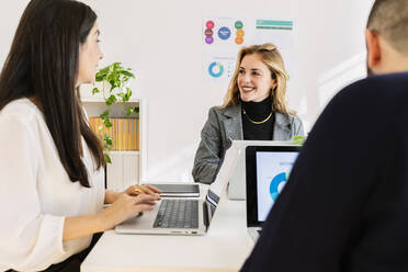 Smiling businesswomen discussing with colleague at desk - XLGF03368