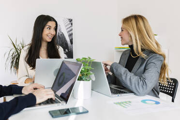 Happy businesswomen having discussion at desk in office - XLGF03371