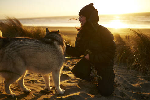 Glückliche junge Frau spielt mit Hund am Strand - ANNF00830