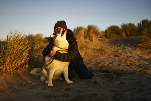 Junge Frau umarmt Husky-Hund auf Sand - ANNF00841