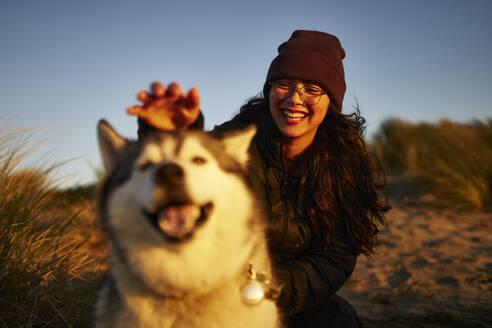 Fröhliche junge Frau hat Spaß mit Hund bei Sonnenuntergang - ANNF00843