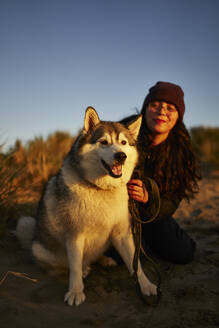 Lächelnde Frau hat Spaß mit Hund bei Sonnenuntergang - ANNF00844