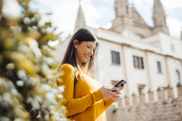 Glückliche Frau mit Smartphone in der Stadt an einem sonnigen Tag - JOSEF23454