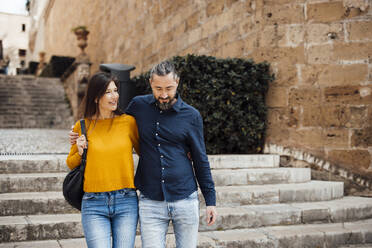 Happy man and woman moving down staircase together - JOSEF23463