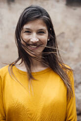 Happy woman wearing yellow t-shirt in front of wall - JOSEF23471