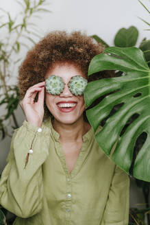 Happy woman with echeveria flowers over eyes near plants - YTF01811