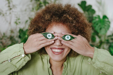 Happy young woman with painted eyes on leaves at home - YTF01823